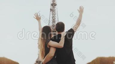 法国巴黎埃菲尔铁塔附近的年轻幸福夫妇。 男人和女人的样子，纪念碑和上升的手。